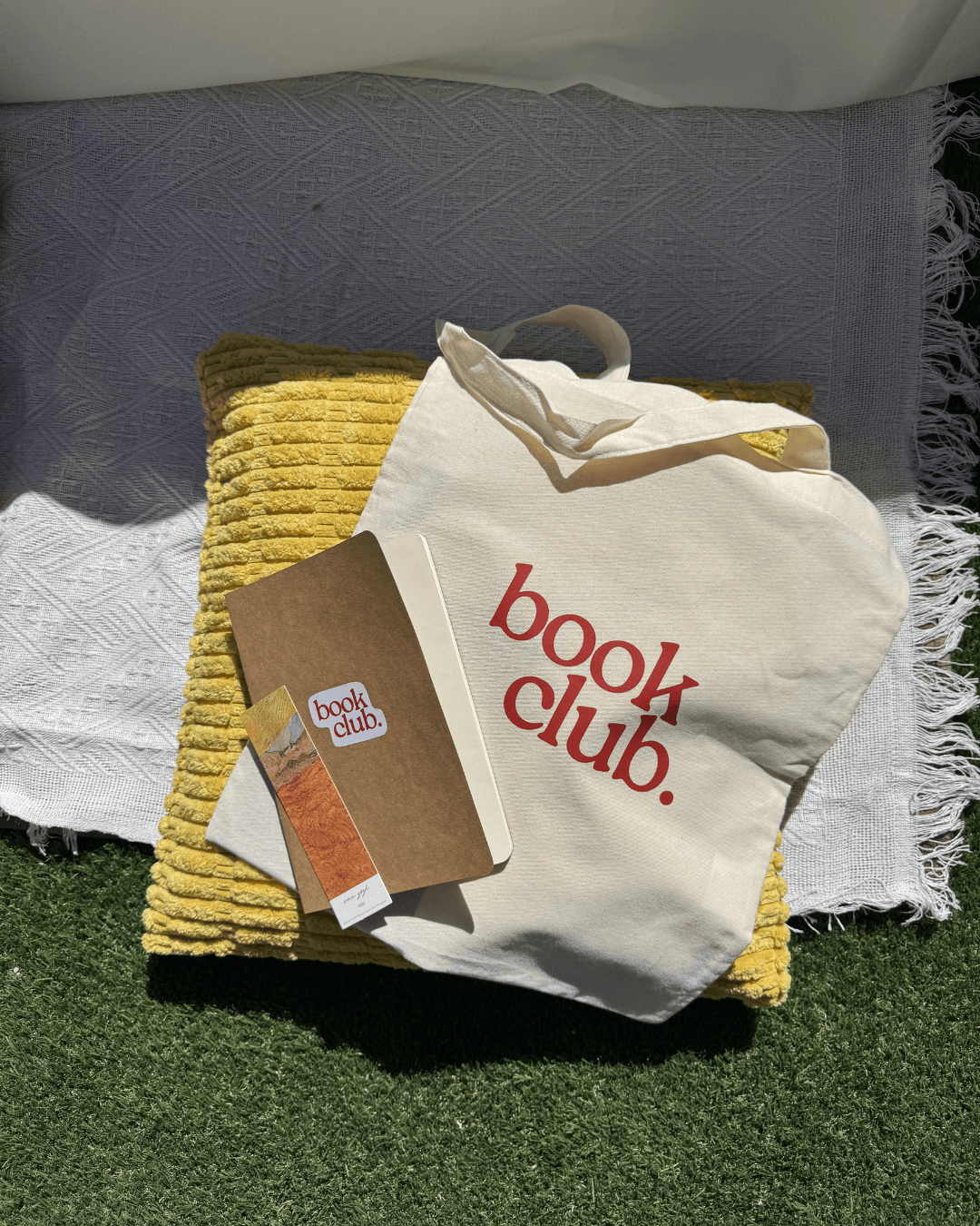 Kit de bienvenida del club: tote bag, libreta y separador sobre cobijas de picnic