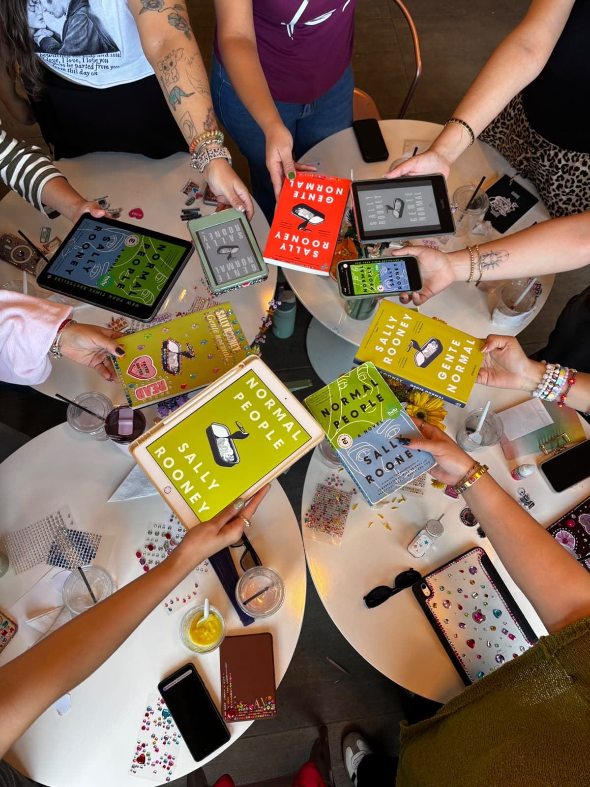 Vista cenital de un círculo de manos sosteniendo sus copias de Normal People de Sally Rooney, físicas y digitales, en el evento de septiembre
