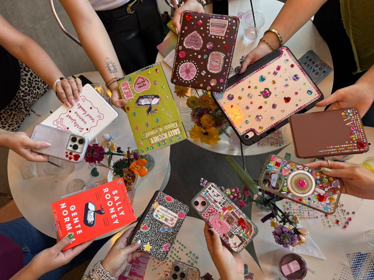 Círculo de manos mostrando las fundas de celular, tablets y el libro que decoraron con pedrería en el evento de septiembre